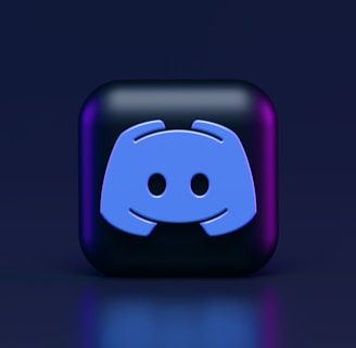 A 3D-style block with a blue logo in the center, set against a dark background. The logo resembles a game controller with two rounded edges and two circles on the front. The block has a subtle gradient, transitioning from dark to purple on its sides.