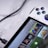A handheld gaming console with a white body and colorful buttons features a screen displaying various game icons. The device is connected to a power source via a black cable and rests on a marble surface. The interface shows games like Apex and Street Fighter.